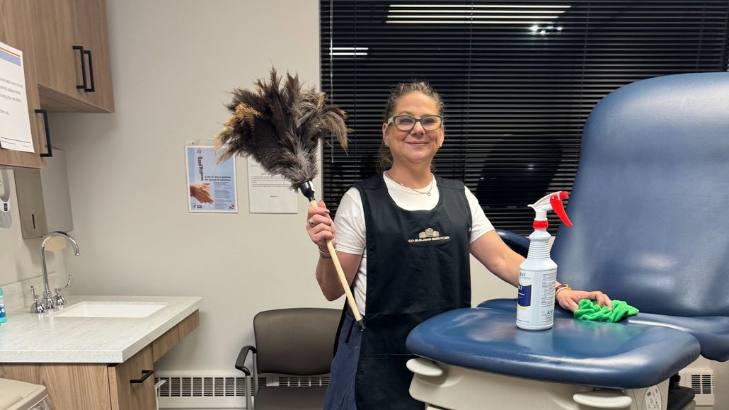 Woman in a salon holds a feather duster beside a chair and cleaning supplies.