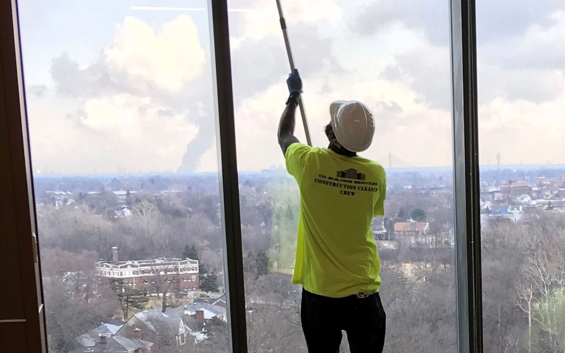 Person in a bright yellow shirt stands by a large window, looking out over a city skyline.
