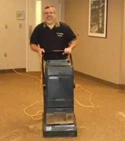 Man standing behind a carpet cleaner in a hallway, holding the handle and smiling.