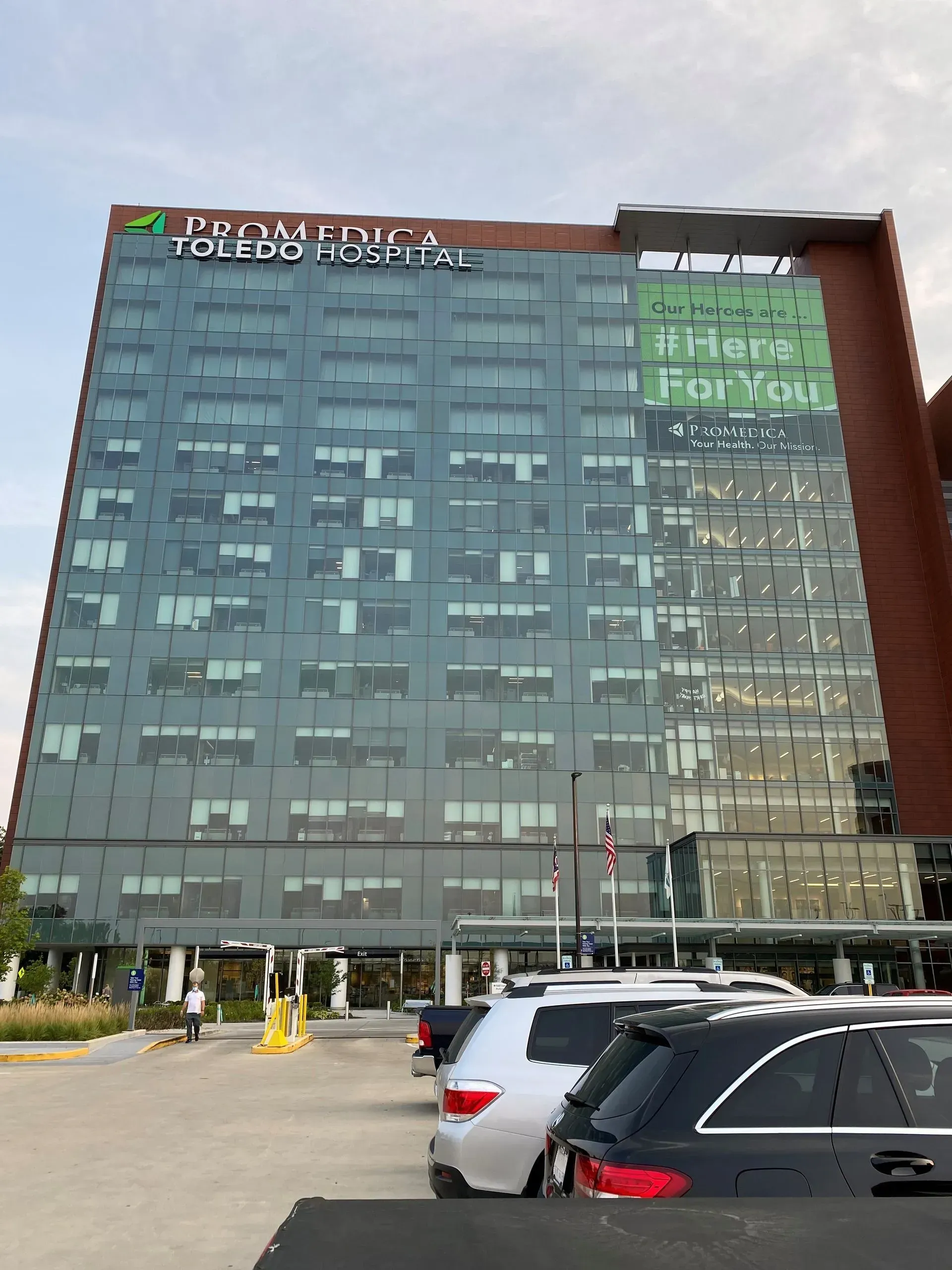 Tall glass hotel building with parked cars in front and a sign near the top.