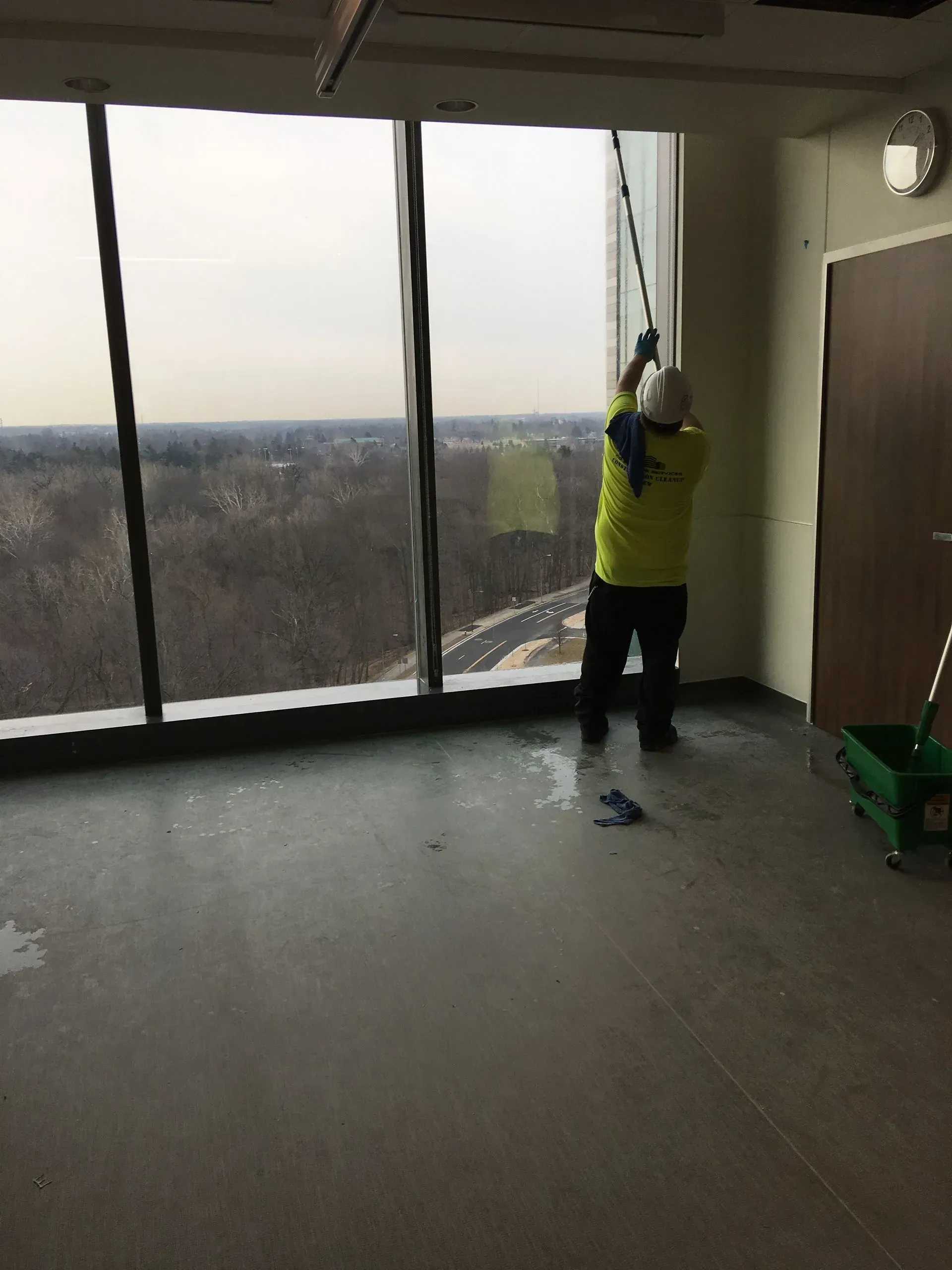 Person in a yellow jacket cleaning tall windows in a room with a city view.