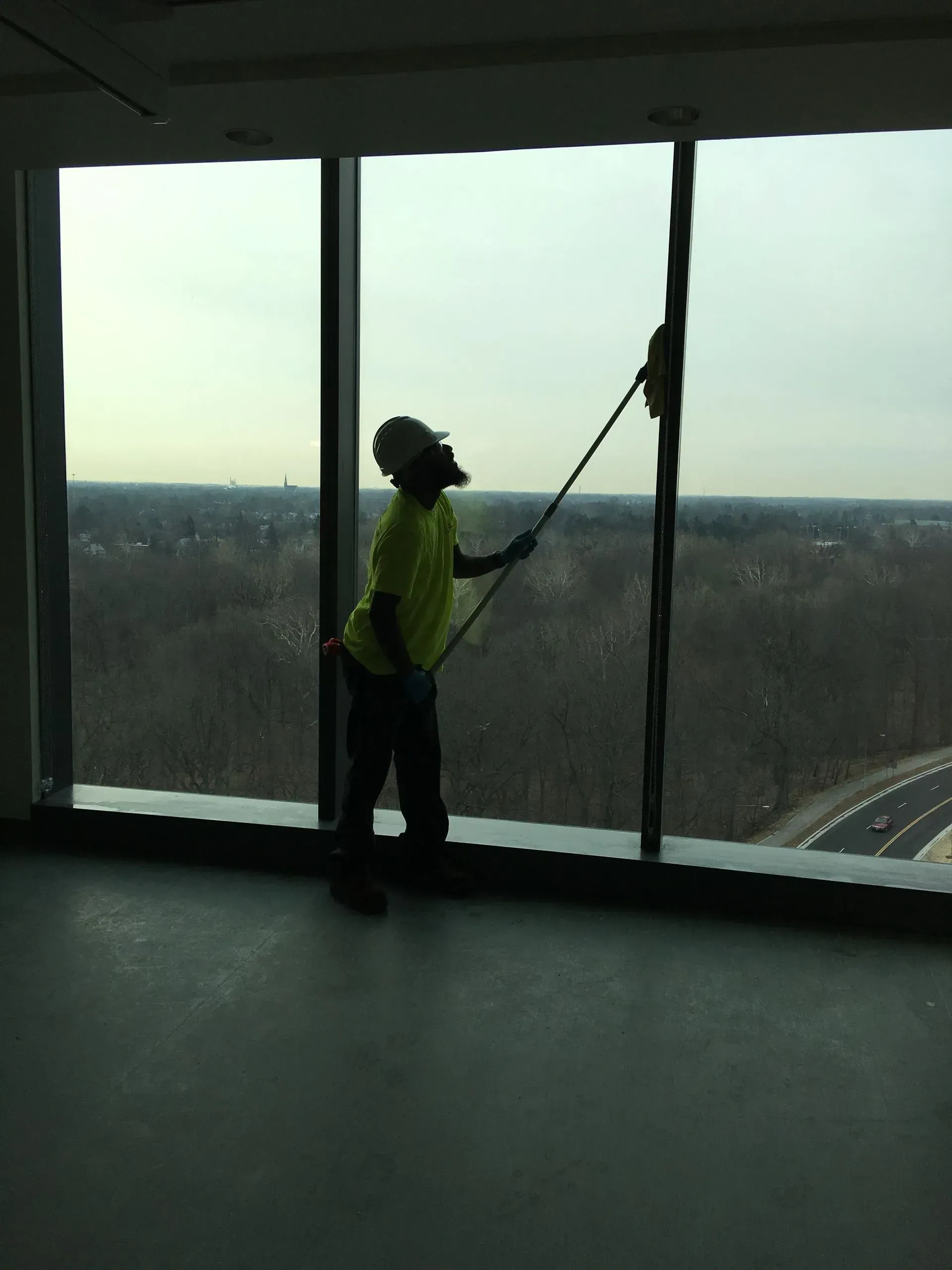 Person in a safety vest cleaning tall windows inside a high-rise building.