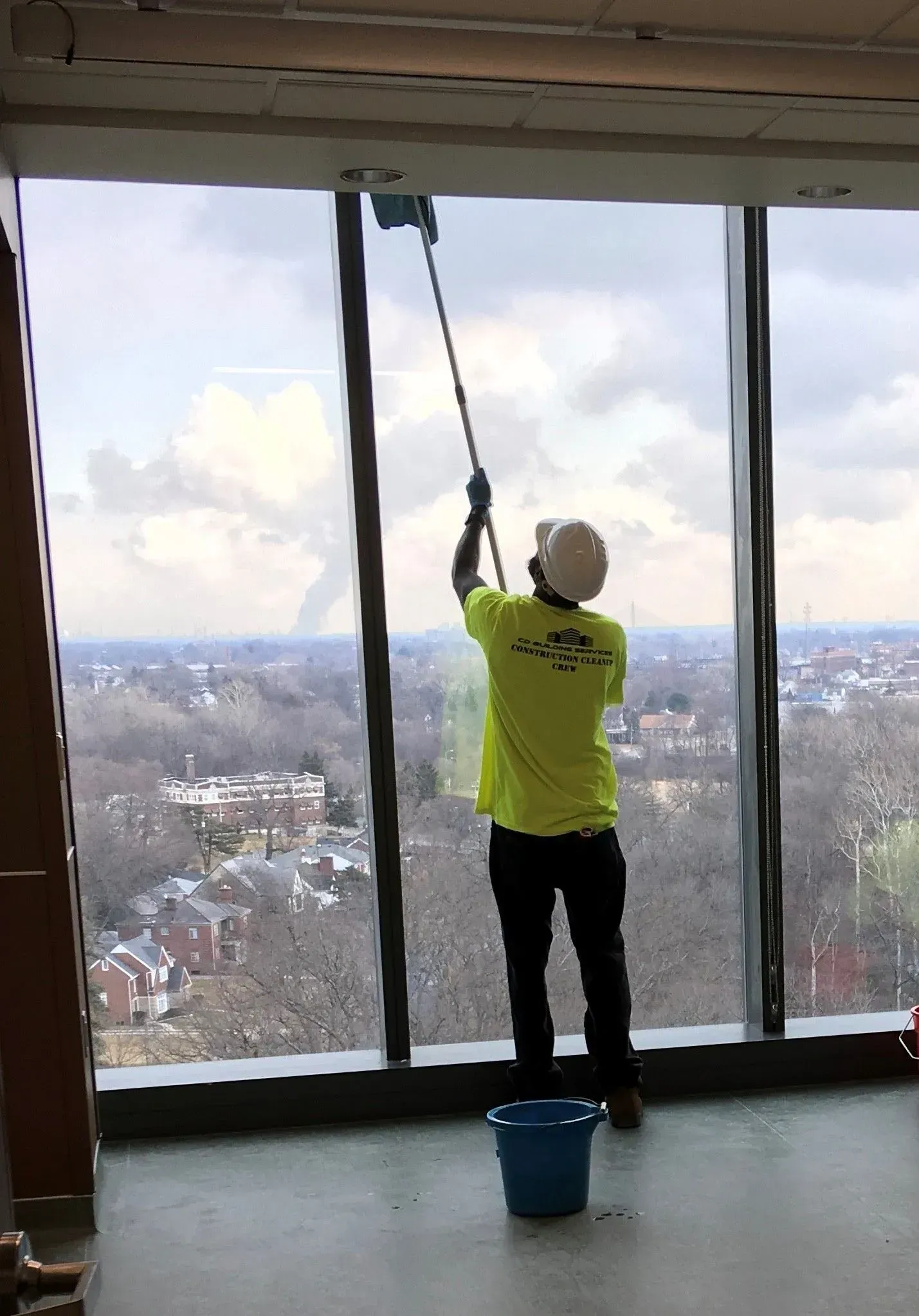 Person in a yellow shirt cleaning a tall window from inside a high-rise apartment.