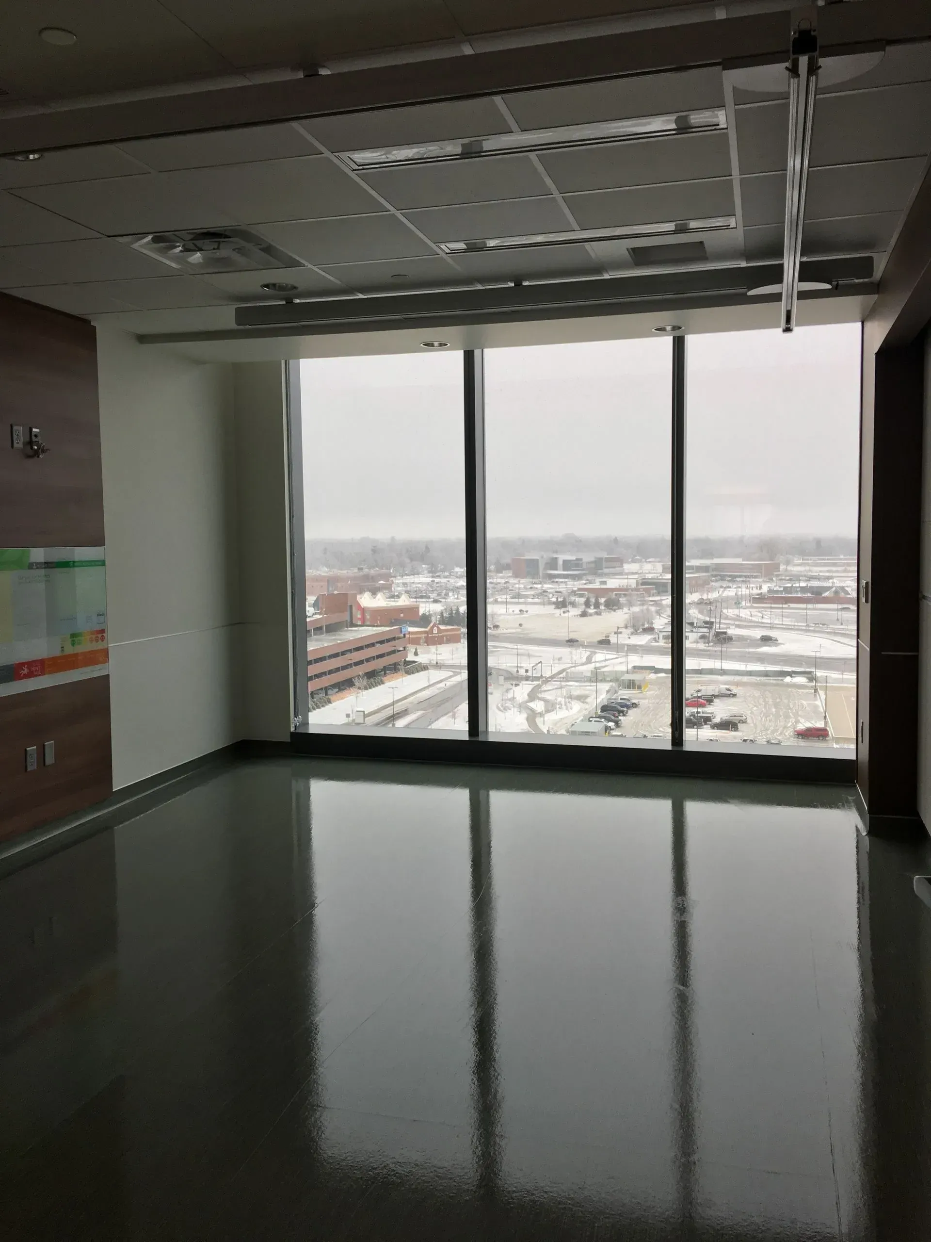 Empty office room with reflective floor and large windows overlooking a snowy cityscape