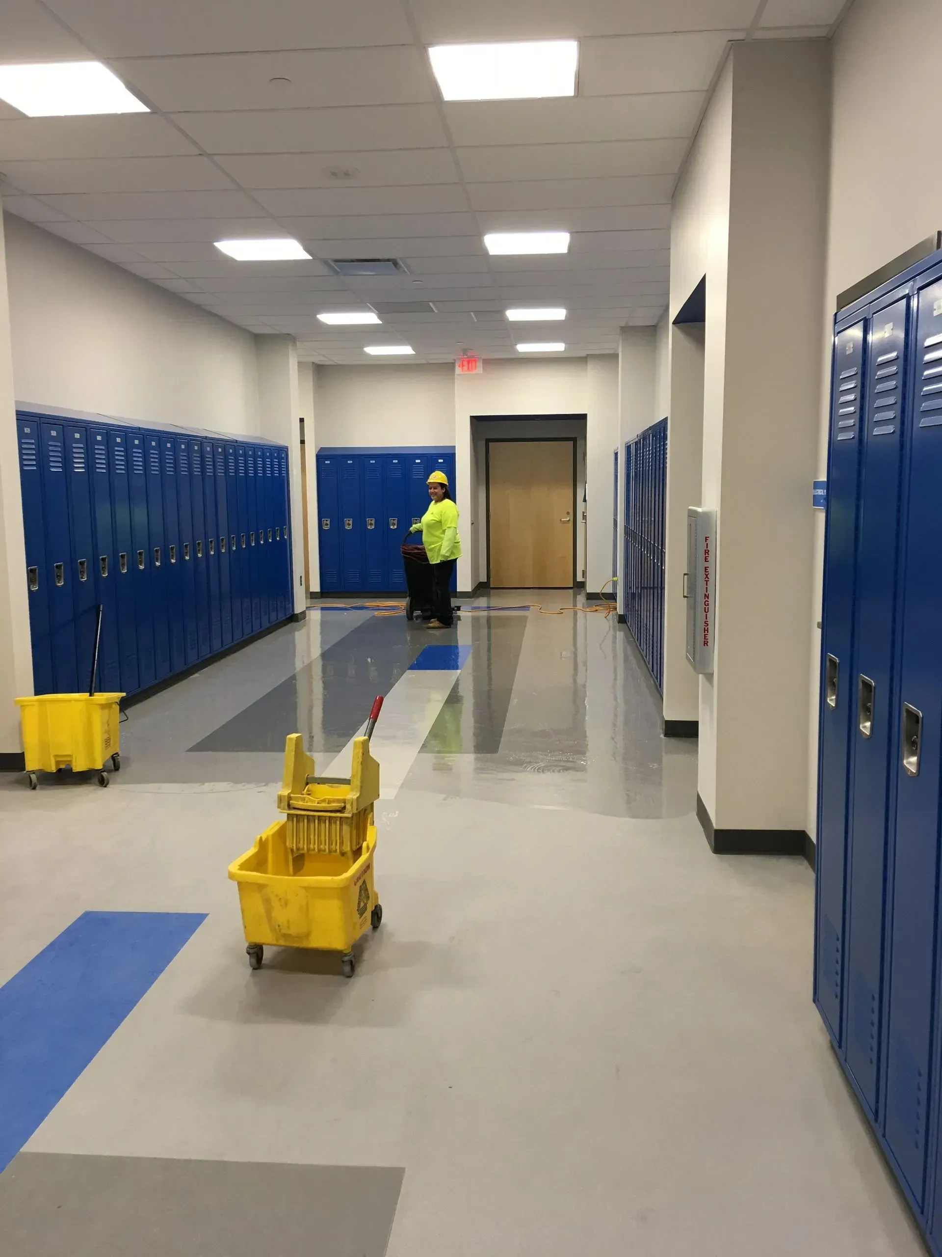 School hallway with blue lockers and yellow wet-floor mops on a freshly mopped floor