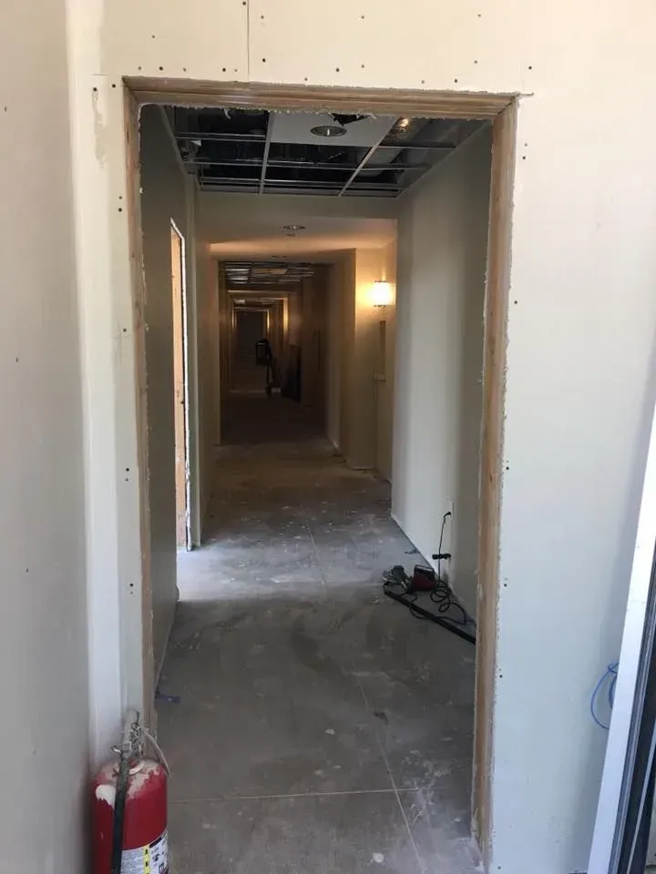 Abandoned hallway under construction with exposed ceiling, bare walls, and a fire extinguisher by the doorway