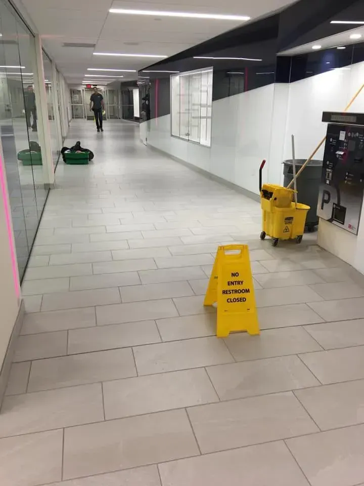 Empty mall corridor with wet floor warning signs, cleaning equipment, and a person in the distance