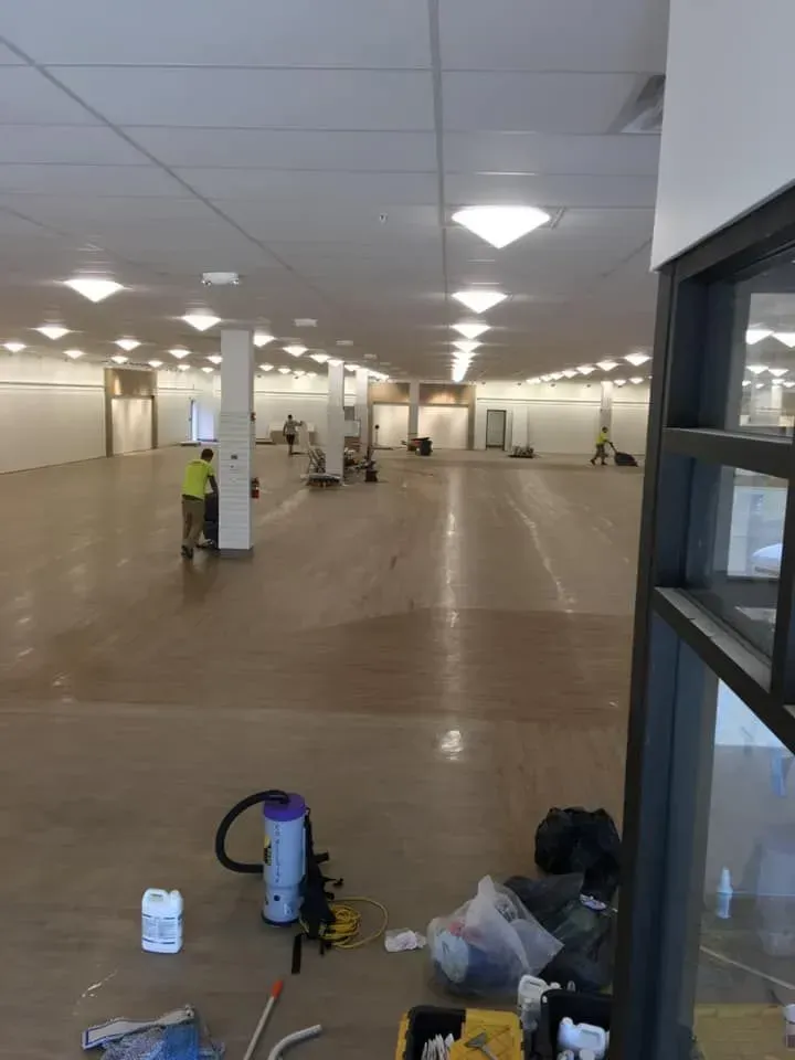 Empty indoor hall with workers, cleaning supplies, and scattered construction tools on the floor