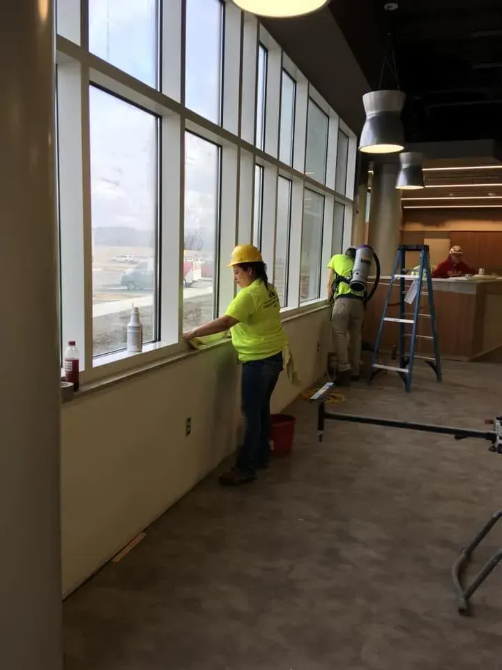 Workers in neon vests installing window coverings inside a large office space