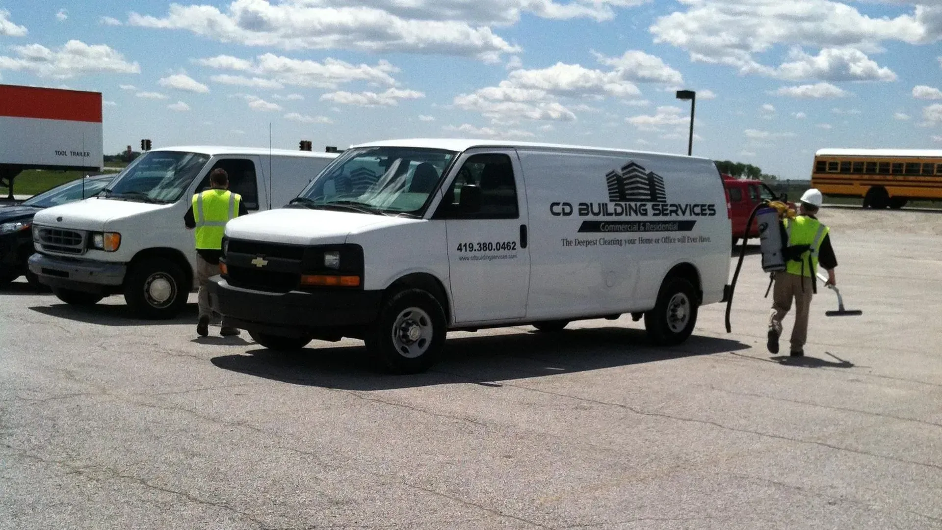White utility van with workers in safety vests parked on a sunny lot near other vehicles.