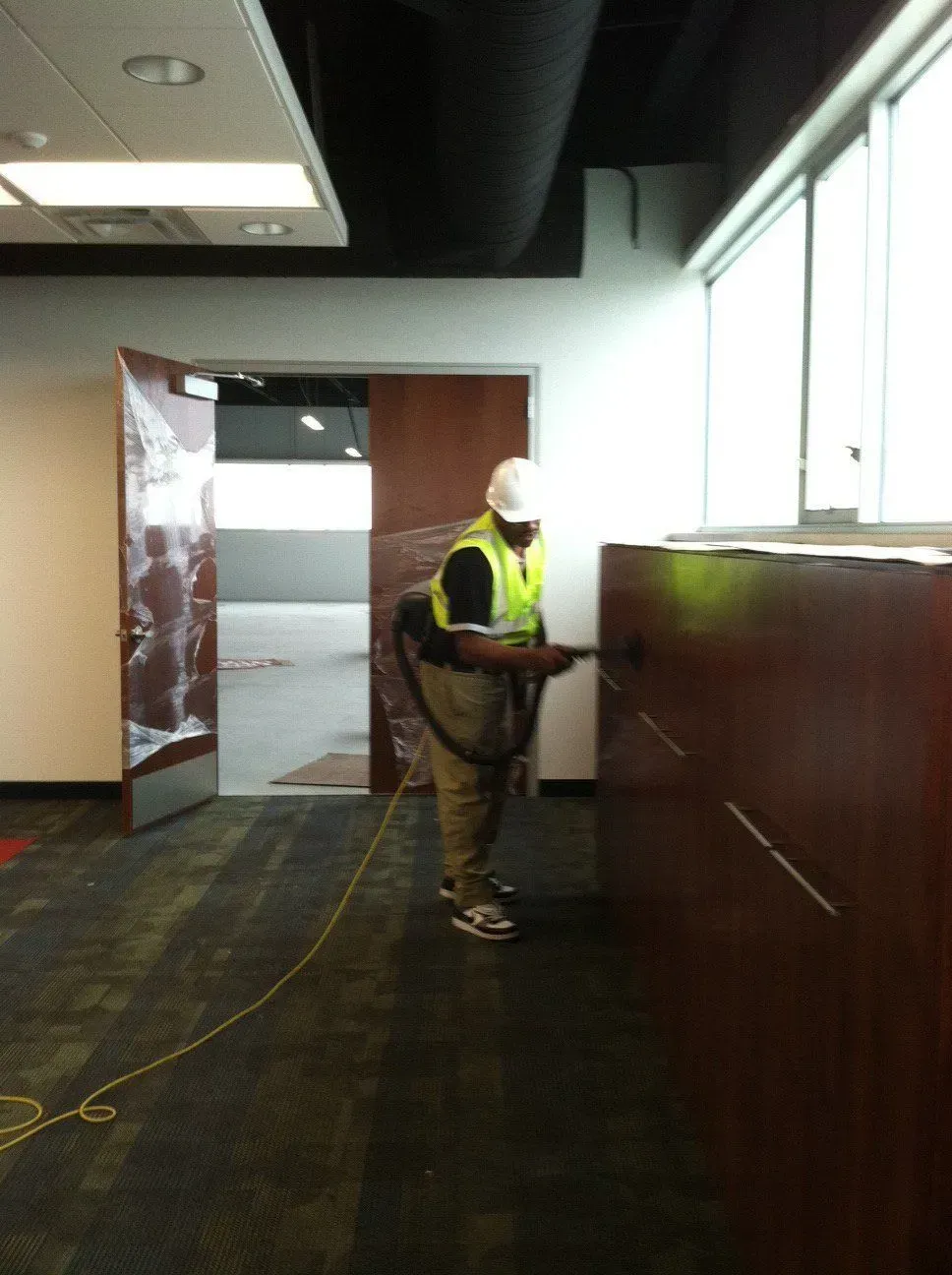 Worker in a neon vest and hard hat using a handheld device beside a reception counter indoors.