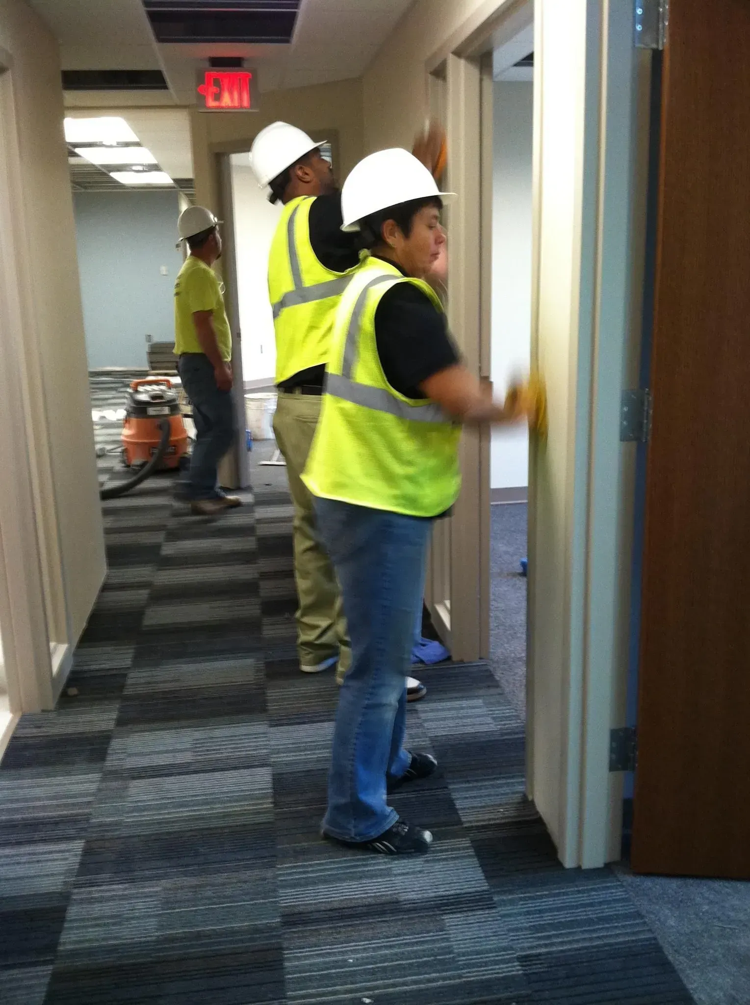 Workers in hard hats and safety vests inspect a hallway under construction.