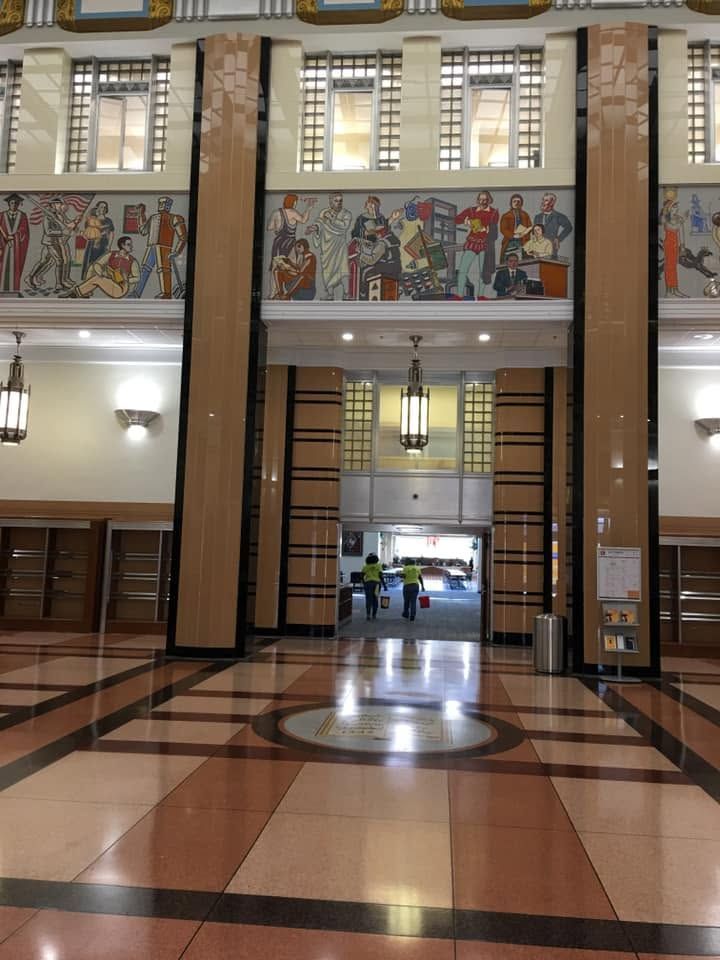 Grand lobby with tall windows, murals, chandeliers, and a polished tiled floor; a few people in the distance