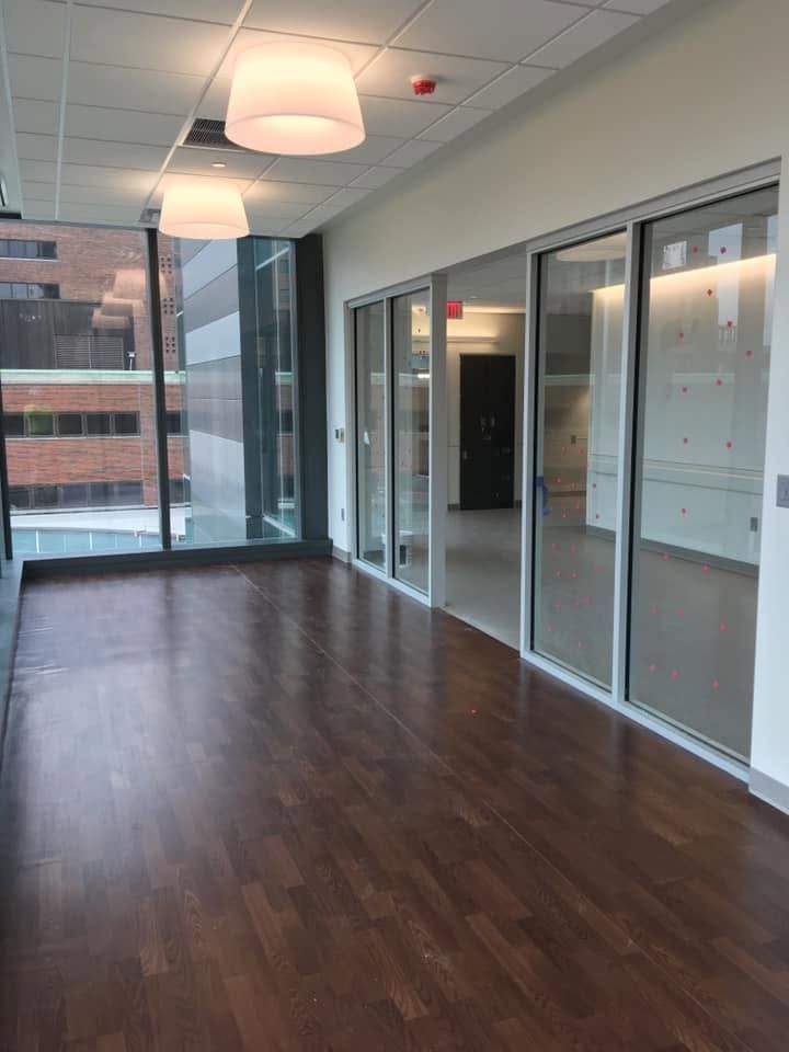 Empty modern office room with glass walls, wood floor, and large windows overlooking buildings