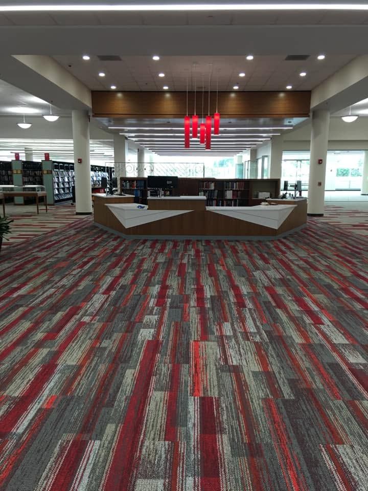 Empty airport lounge with red patterned carpet, wooden seating islands, and large windows in the background