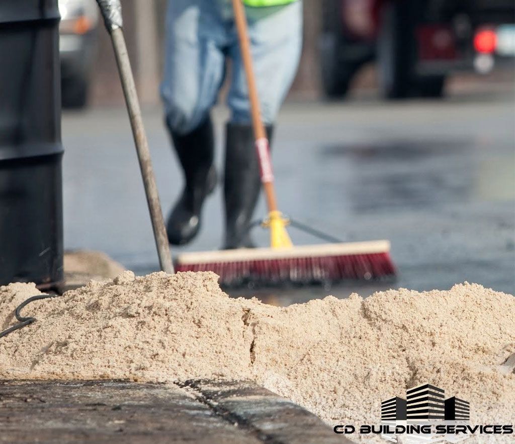Workers sweeping loose sand off a wet road with brooms
