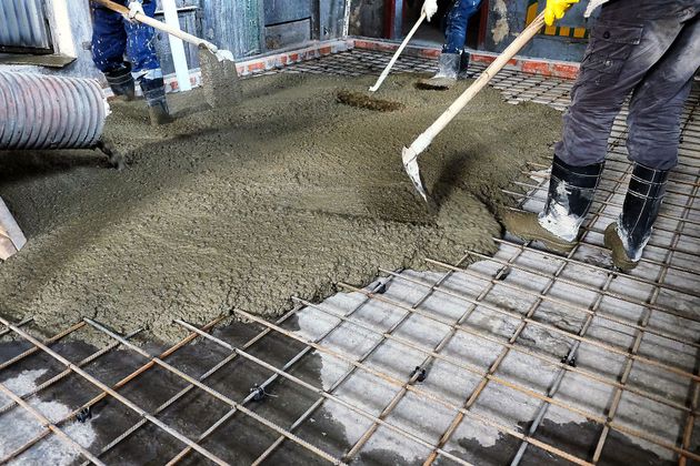 Workers pouring wet concrete over rebar at a construction site.