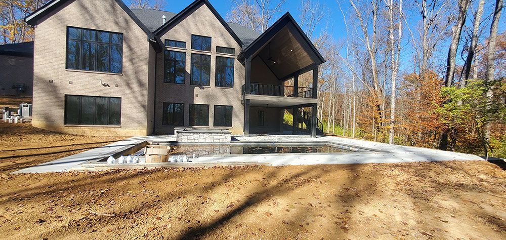 Modern dark-gray house under construction with a curved concrete driveway and bare trees in front