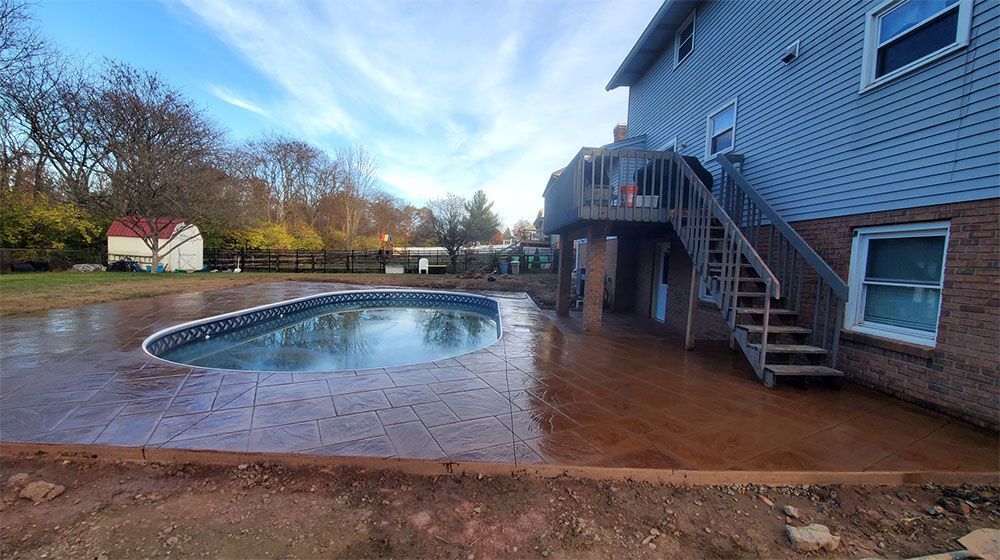 Backyard pool beside a house with a wet brick patio and wooden deck stairs