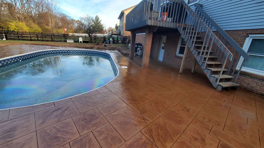 Backyard pool beside a brown stamped-concrete patio and exterior staircase under an overcast sky