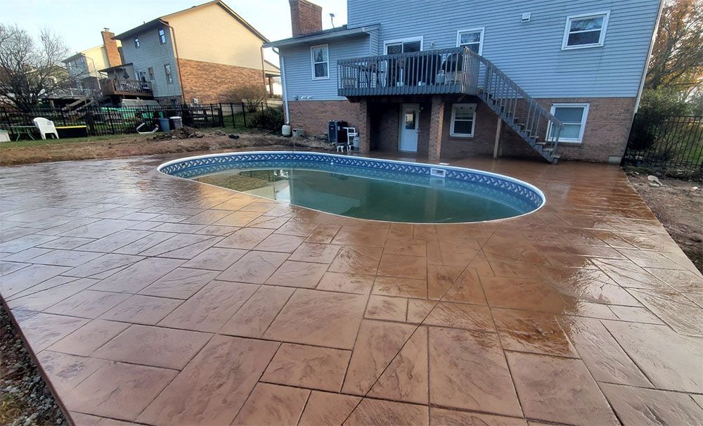 Backyard patio with a small covered pool and wet stamped concrete near a house.