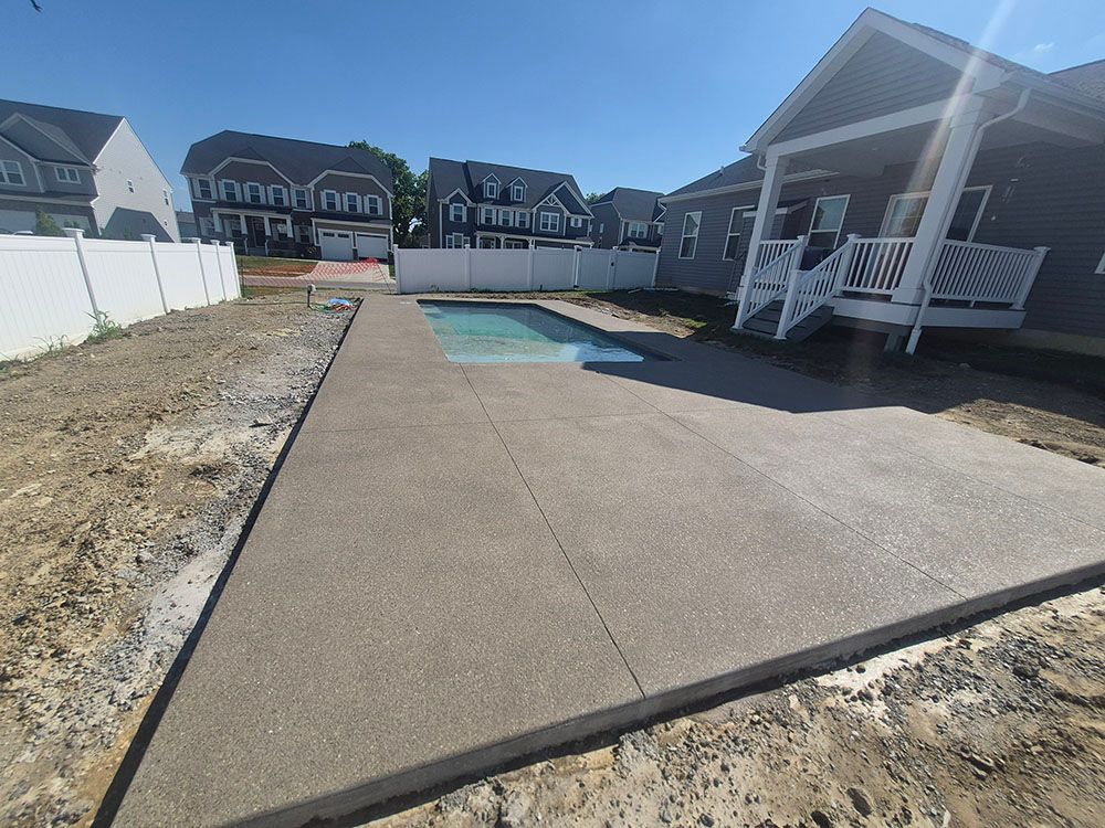 Backyard with a concrete pool deck beside an in-ground pool and covered patio, surrounded by houses.