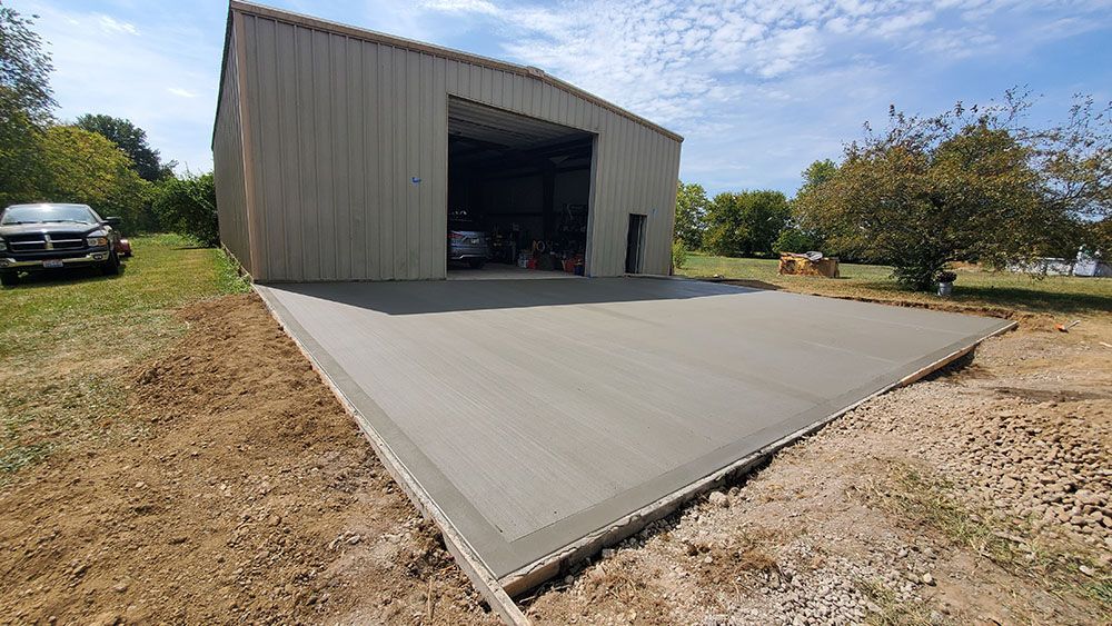 Large concrete ramp leading to an open metal garage building in a rural yard