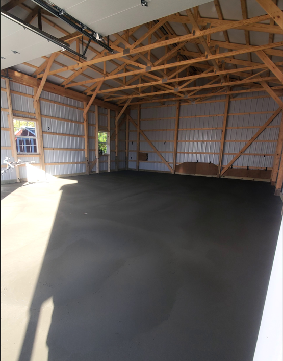 Empty wooden barn interior with exposed trusses and a dark concrete floor
