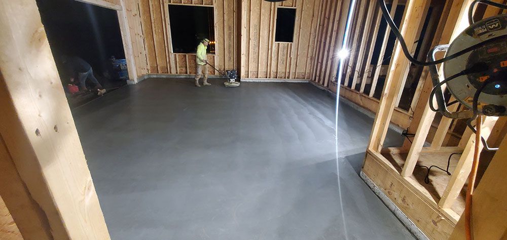 Unfinished room with exposed wooden studs and a smooth gray floor; a worker stands near the back wall.