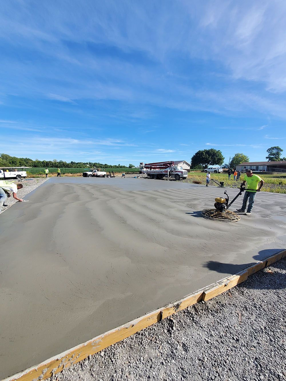 Workers smoothing fresh concrete at a construction site under a blue sky