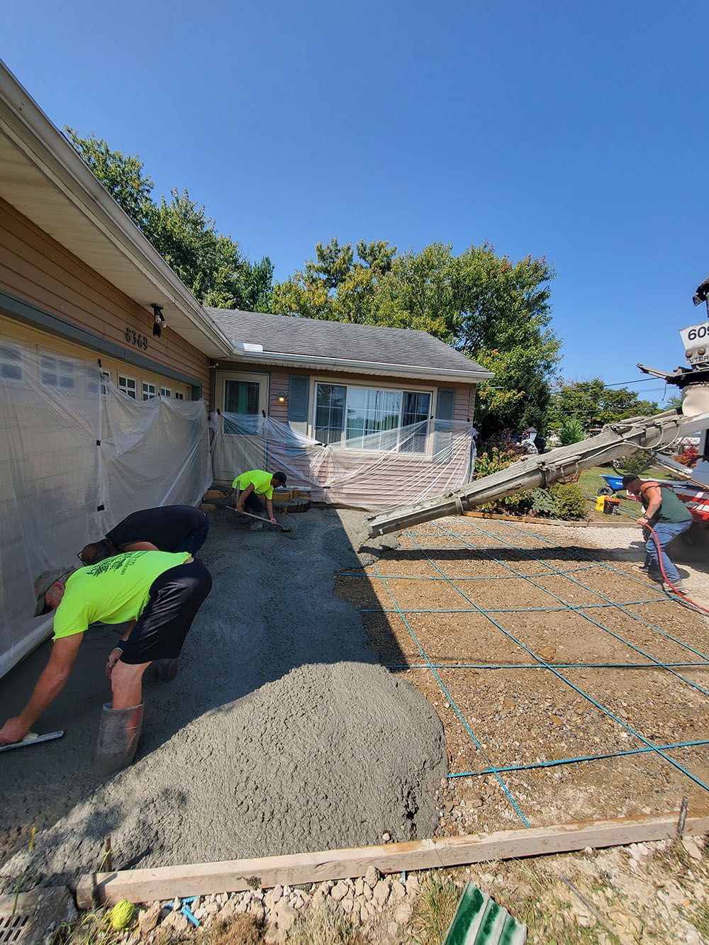 Workers spreading gravel in a sloped residential driveway beside a garage and house under a clear blue sky