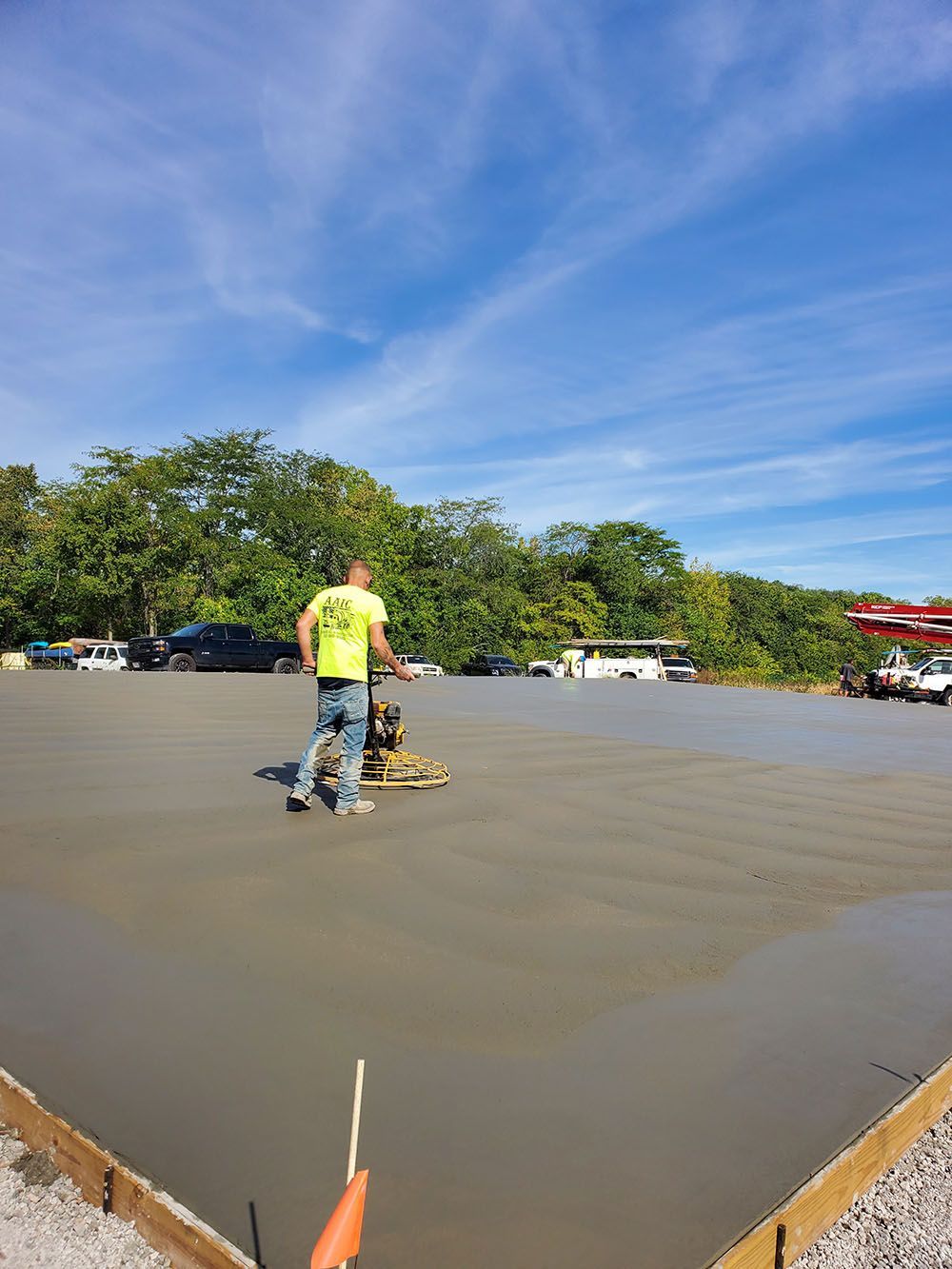Worker smoothing fresh concrete in a parking lot under a blue sky