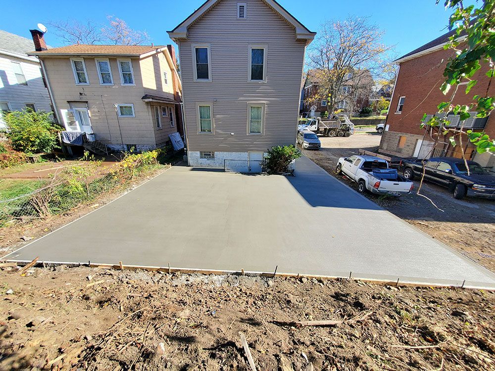 New concrete driveway beside a gray house, with a parked white car and neighboring homes.