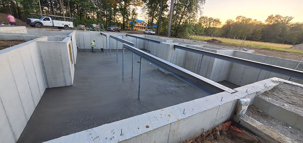 Concrete basement foundation under construction at sunset, with rebar and support walls.