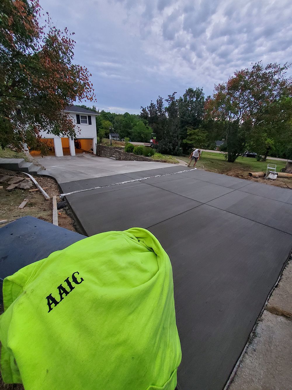 Bright green bag in foreground on a driveway with trees, a house, and an overcast sky.