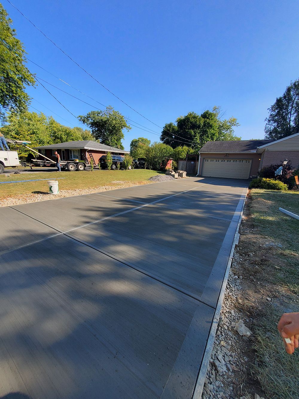 Quiet residential street with a wide paved road, houses, trees, and a clear blue sky