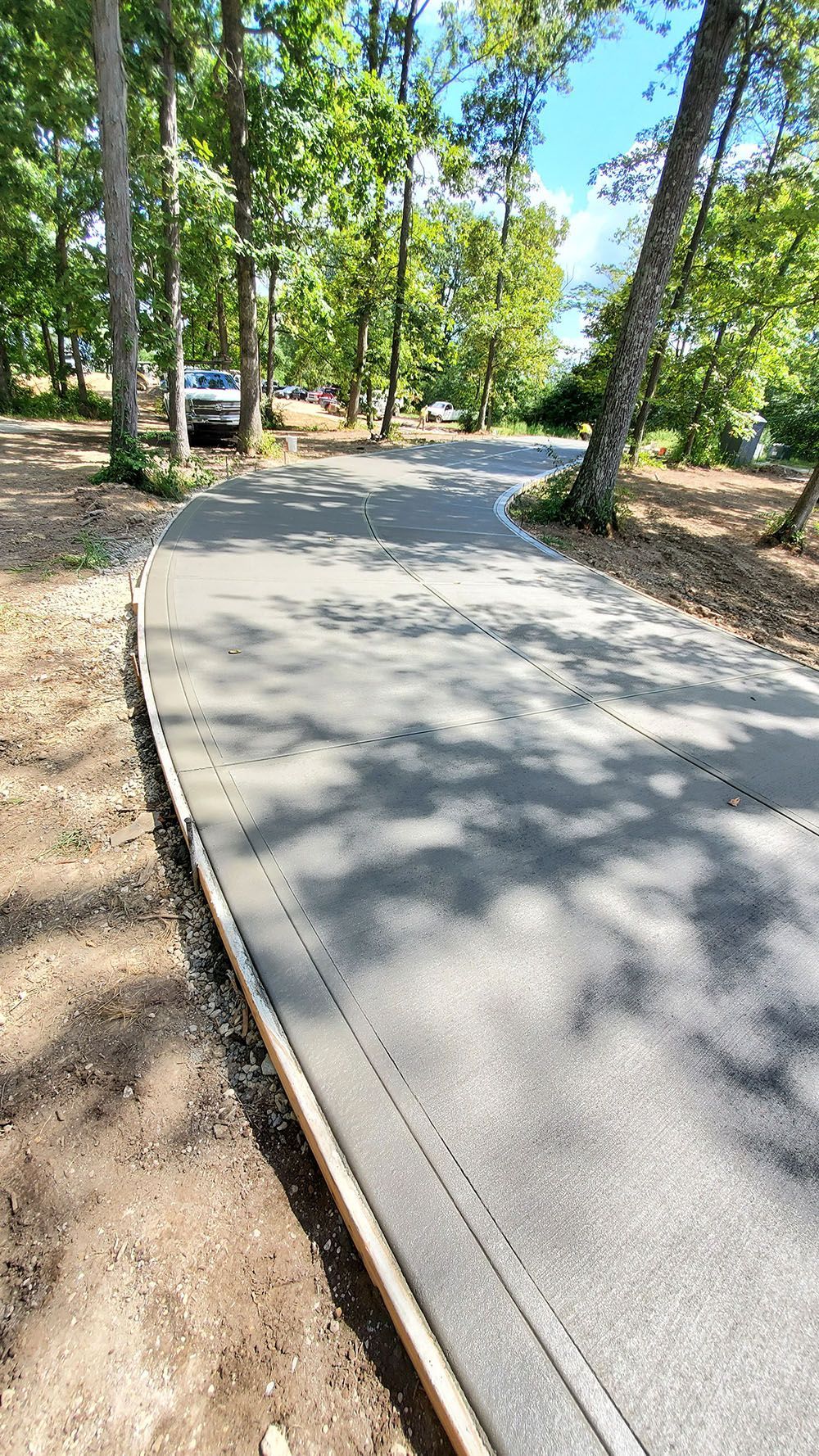 Curved paved path through a wooded park, with a parked car visible ahead on the left.