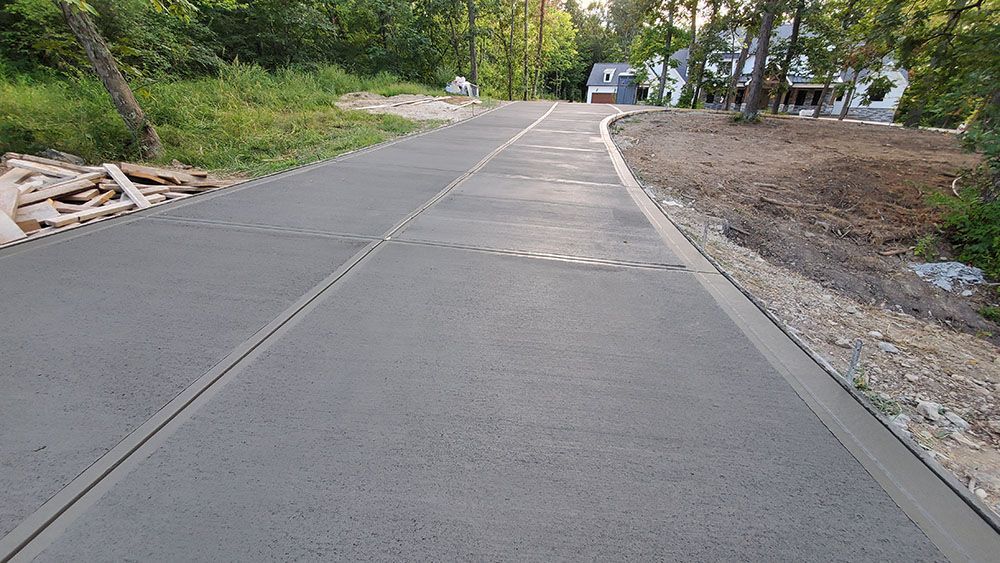 Freshly poured concrete road through a wooded area with gravel shoulders and a stop sign in the distance