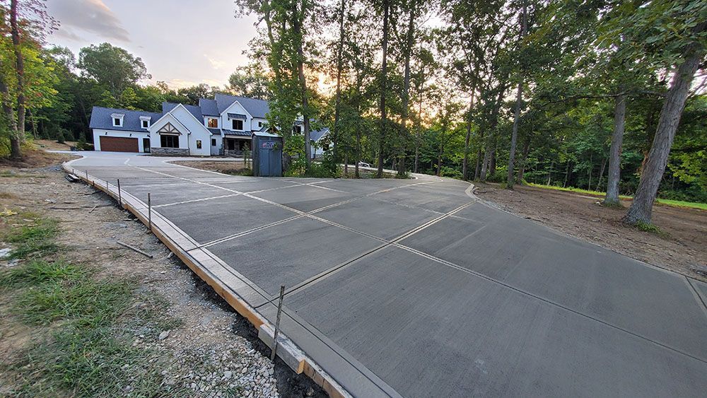 Concrete driveway under construction beside a white house at dusk, with trees and a utility pole nearby