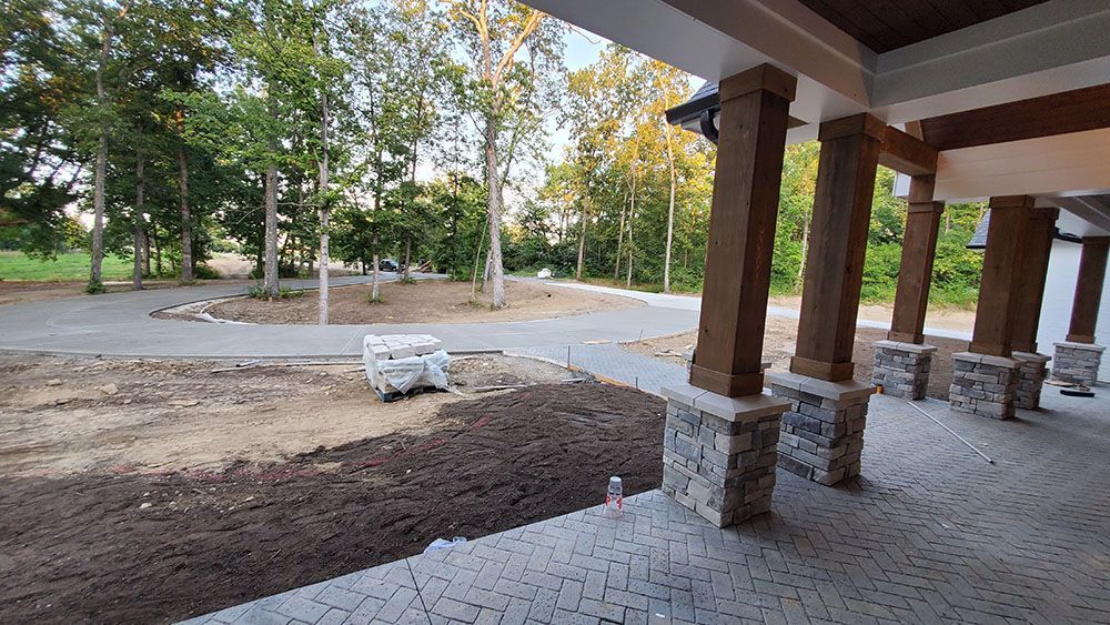Covered patio with stone columns overlooking a gravel and dirt landscaped yard with trees in the background
