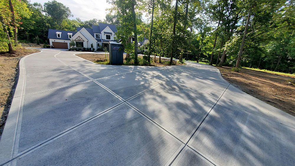 Concrete driveway with expansion joints leading to a house and trees on a sunny day