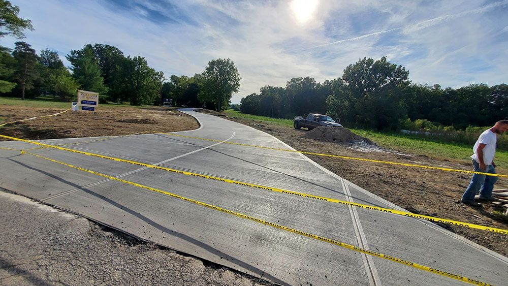 Freshly paved curved road with yellow caution tape, dirt shoulders, and a person standing at the right edge