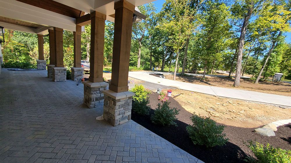 Covered brick walkway with stone columns overlooking a landscaped road and trees