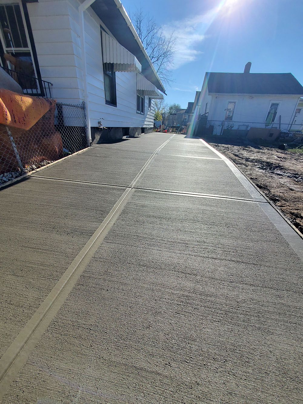 Concrete driveway between houses under bright sun with a blue sky and lens flare