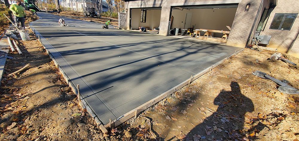 Freshly poured concrete driveway beside a house, with a worker’s shadow in the foreground