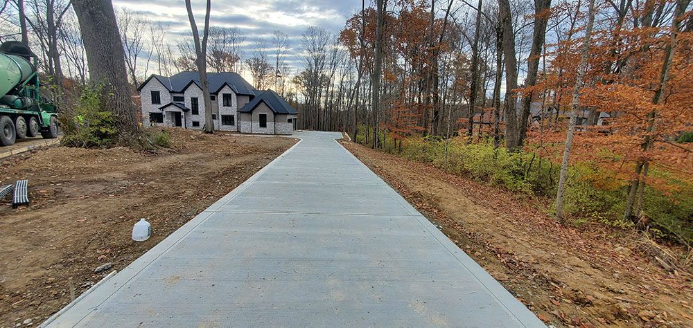 Concrete driveway leading to a house through a wooded yard with autumn trees