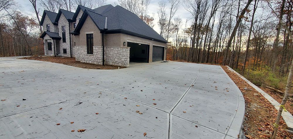 Modern stone-and-stucco house with a wide concrete driveway and autumn trees nearby