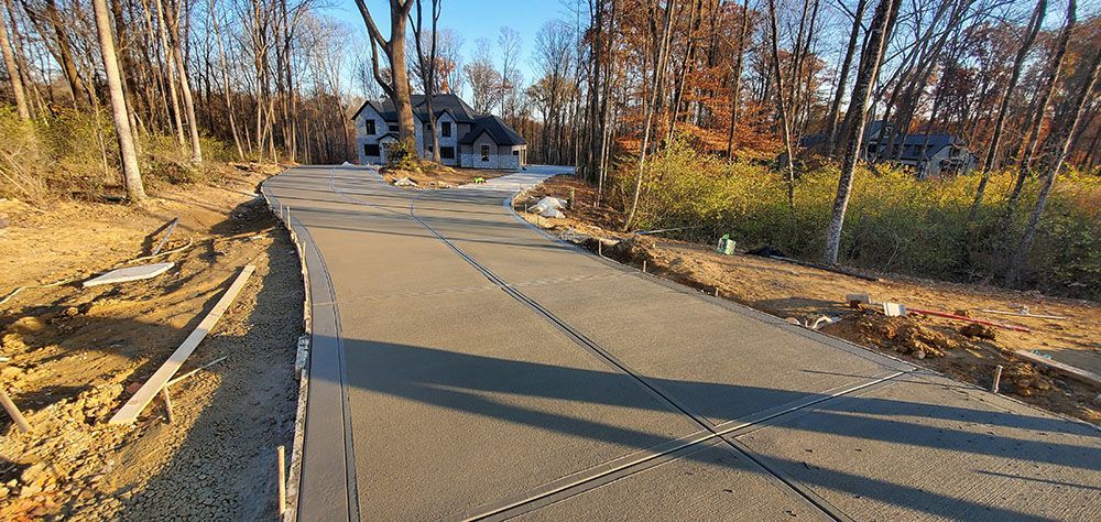 Curved rural road under construction with fresh asphalt, traffic cones, and leafless trees on both sides