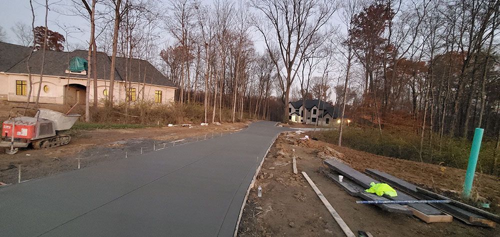 Rural road curves past a house and bare trees, with roadwork materials and a wet shoulder on the right.