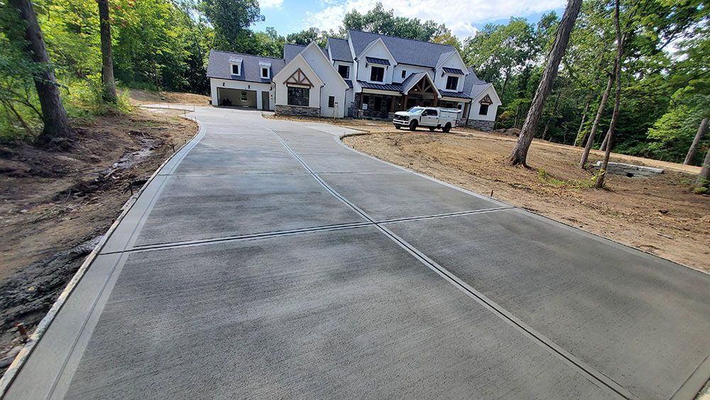 New concrete driveway leading to a large house under construction in a wooded area